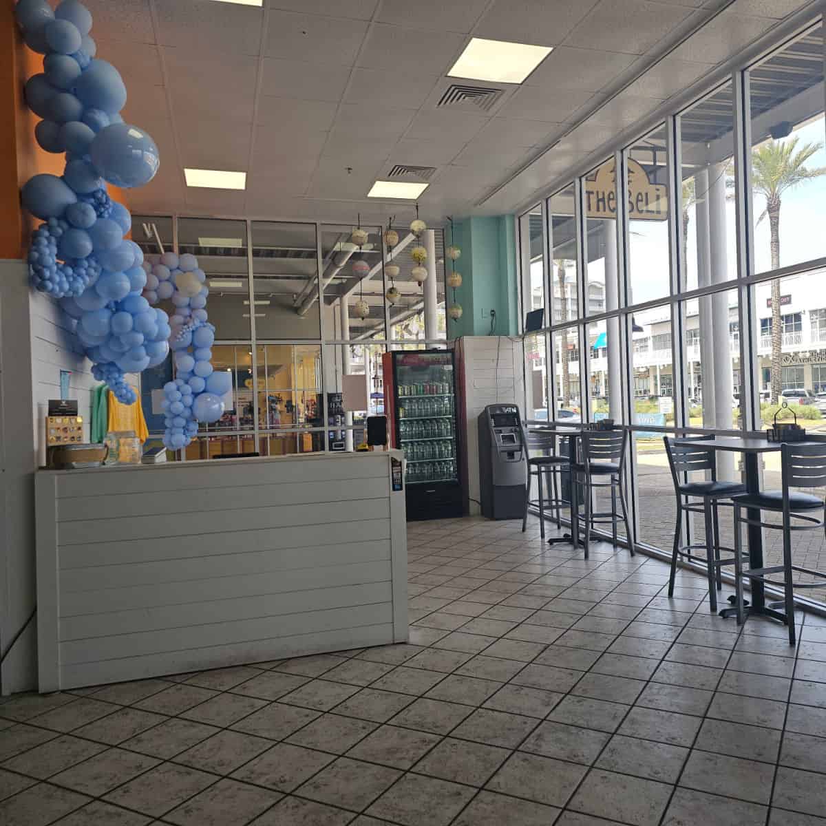 beli deli interior with large windows on the right side, blue balloons on the left side and an order counter by the left wall