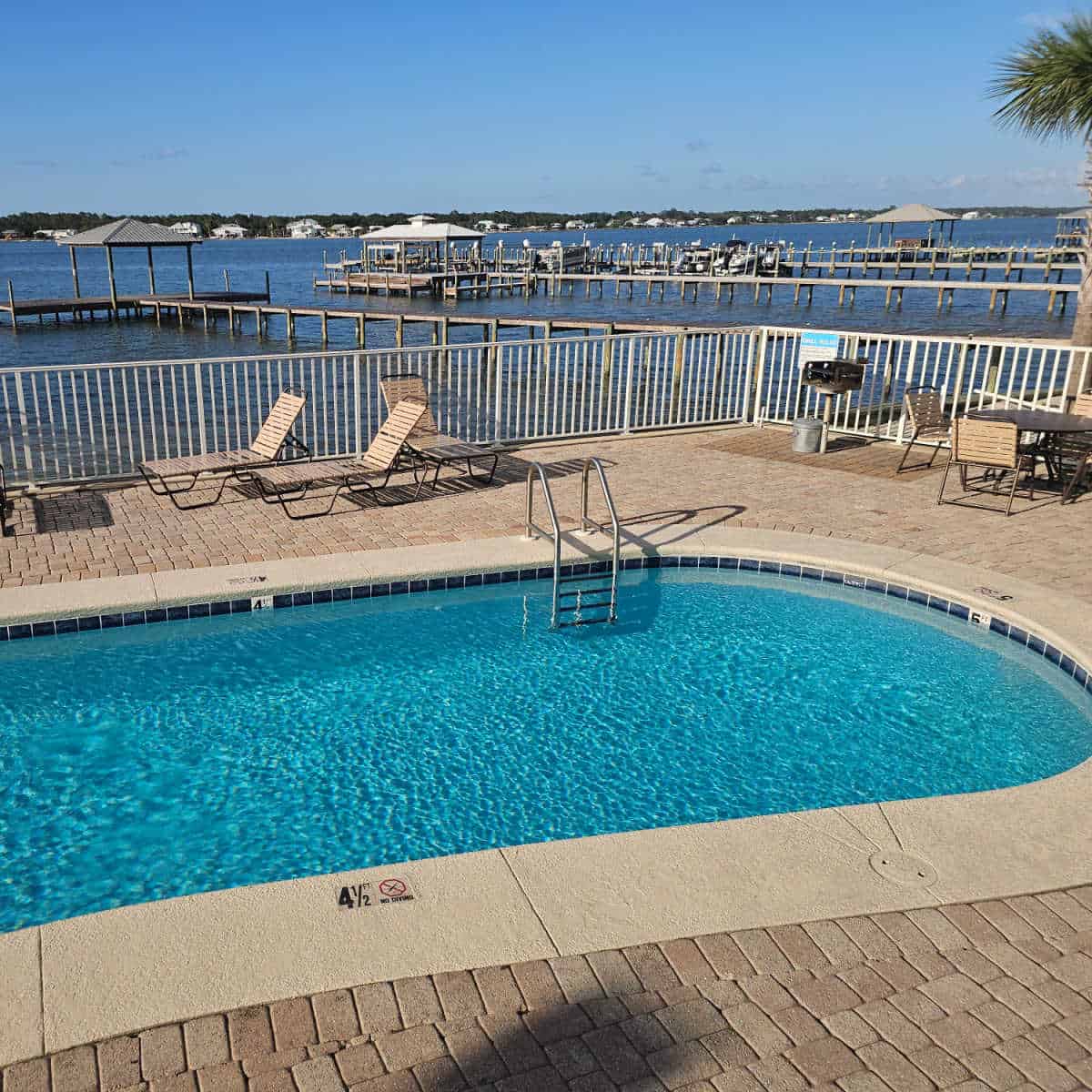Outdoor pool with paved deck, lounge chairs along the deck along with a barbecue and metal can and fence with Little Lagoon in the background at Lagoon Tower