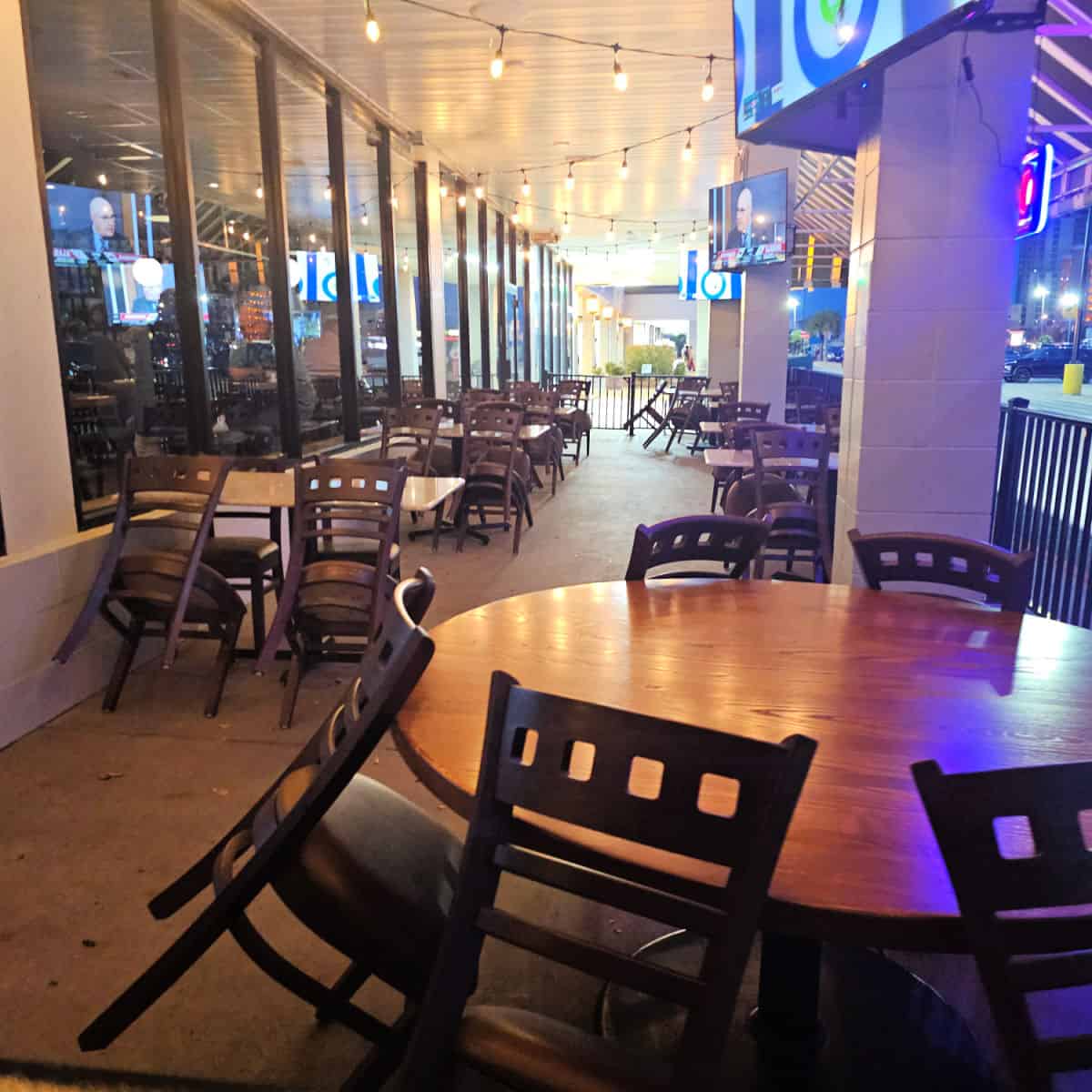 outdoor seating with tables and chairs, tvs hanging on the pilars