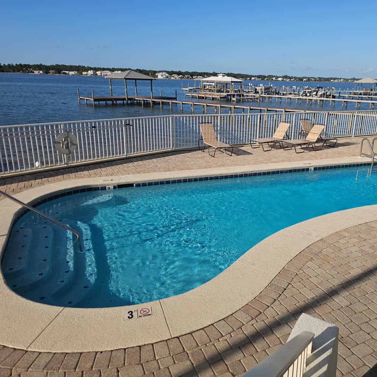 Outdoor pool with paved deck, lounge chairs along the deck and fence with Little Lagoon in the background at Lagoon Tower