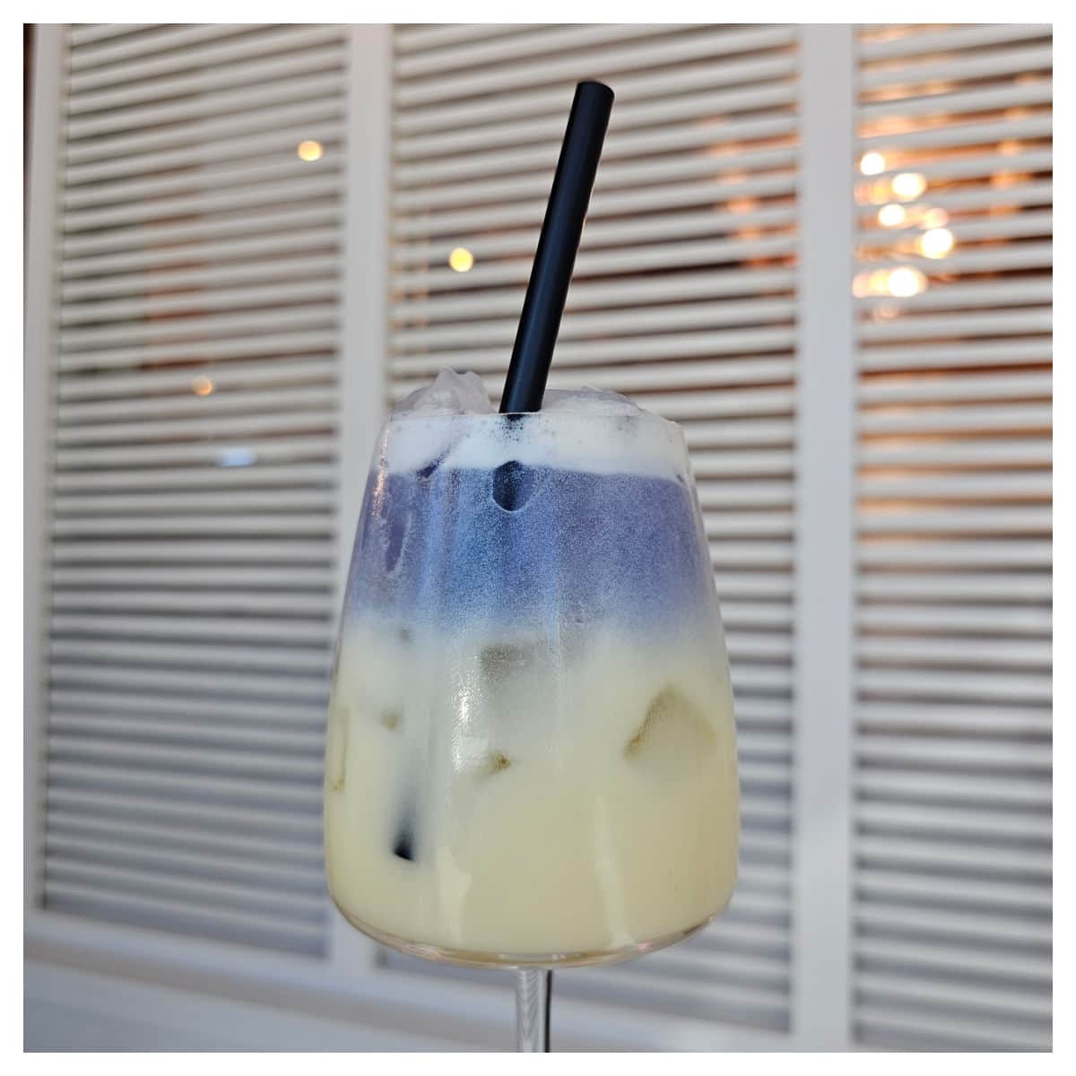 Layered purple and cream colored drink in a glass next to white shutters