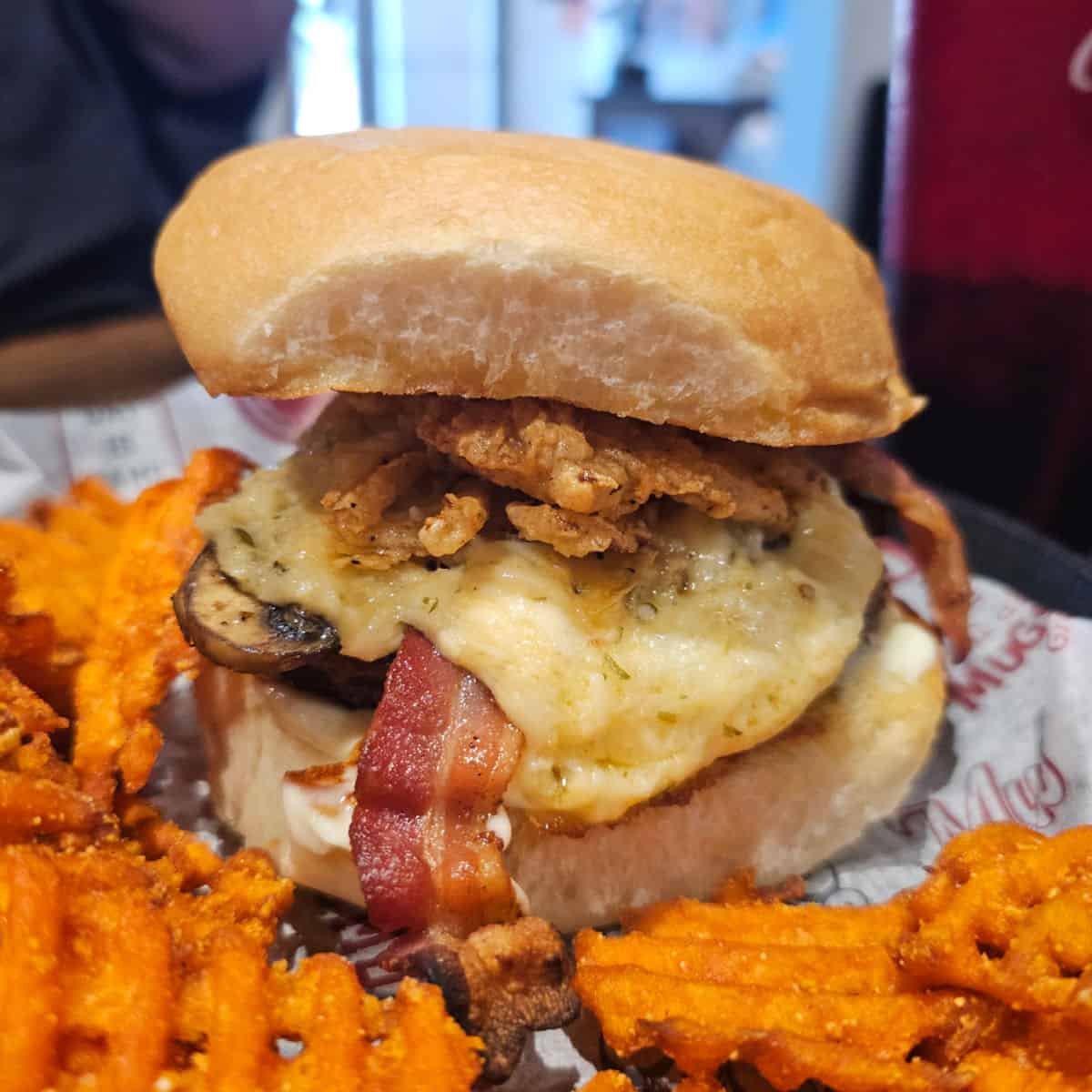 burger with bacon, melty cheese, and mushrooms next to sweet potato fries