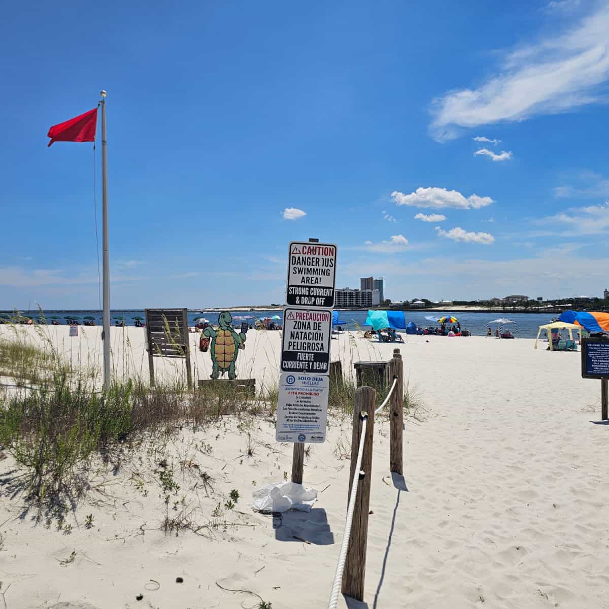 Single red beach warning flag over Dangerous swimming area strong current sign, beach umbrellas set up on the beach