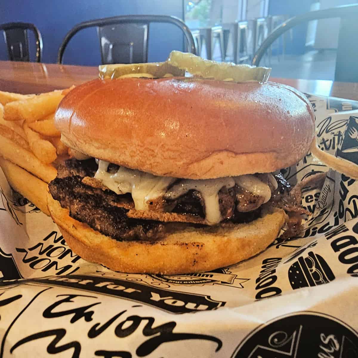 mushroom swiss burger with a pickle on top next to fries in a paper lined basket