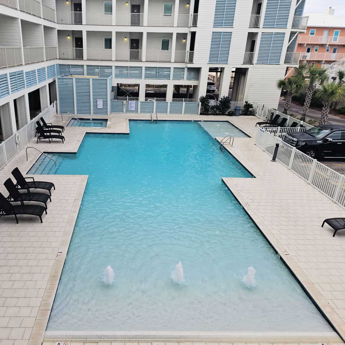 resort style pool with zero entry area with three small fountains, lounge chairs around the pool, small hot tub in the corner