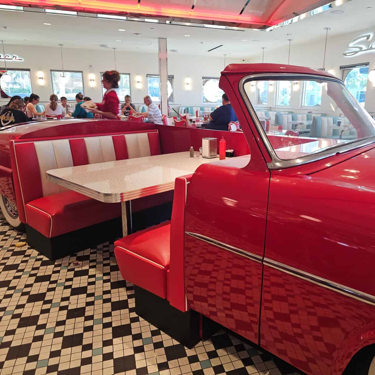 retro red car with booth seating, people sitting behind the car with Sunliner sign on the wall, waitress walking by