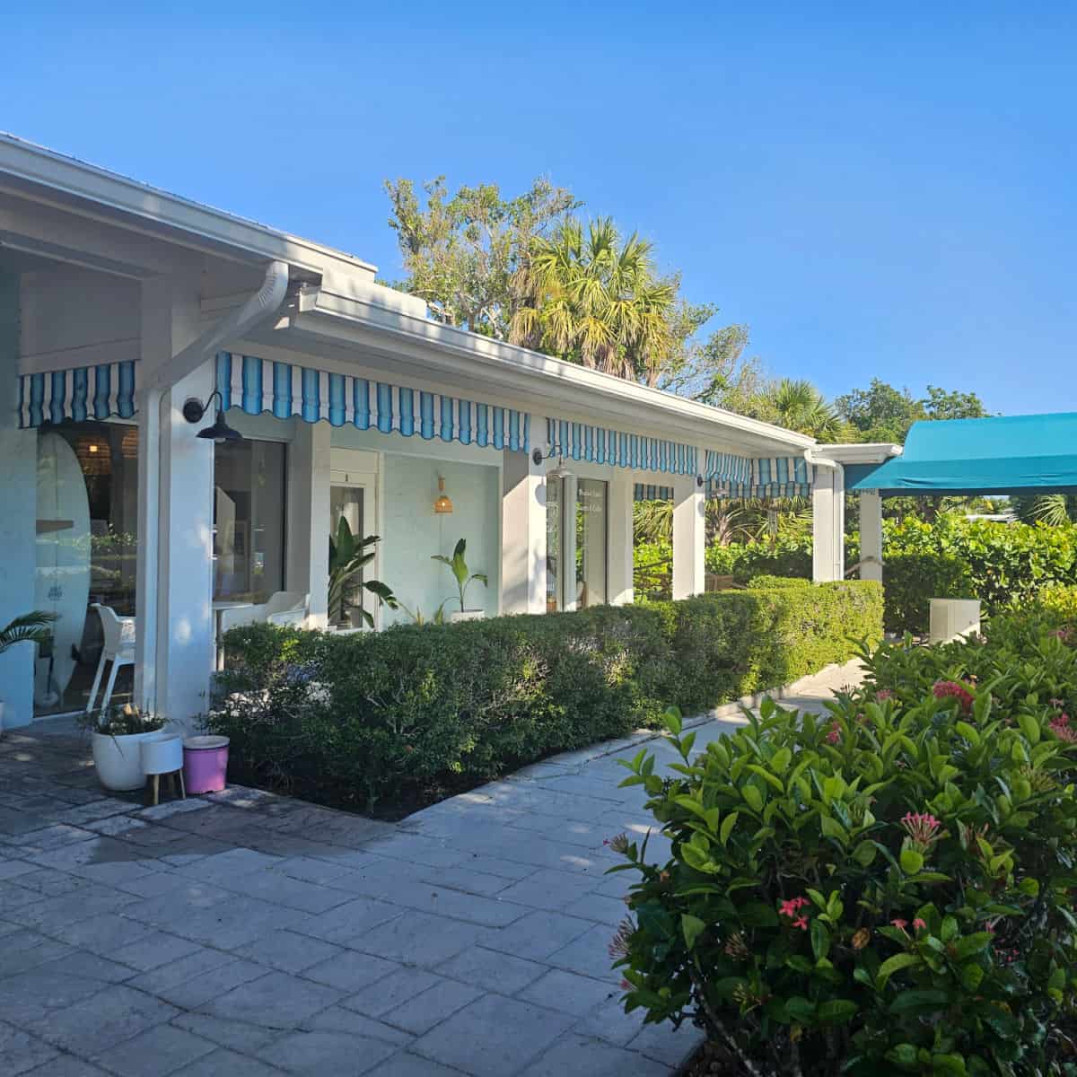 white building with a blue and white awning, surfboard in the window, plants lining the walkway to the Sanibel Sprout