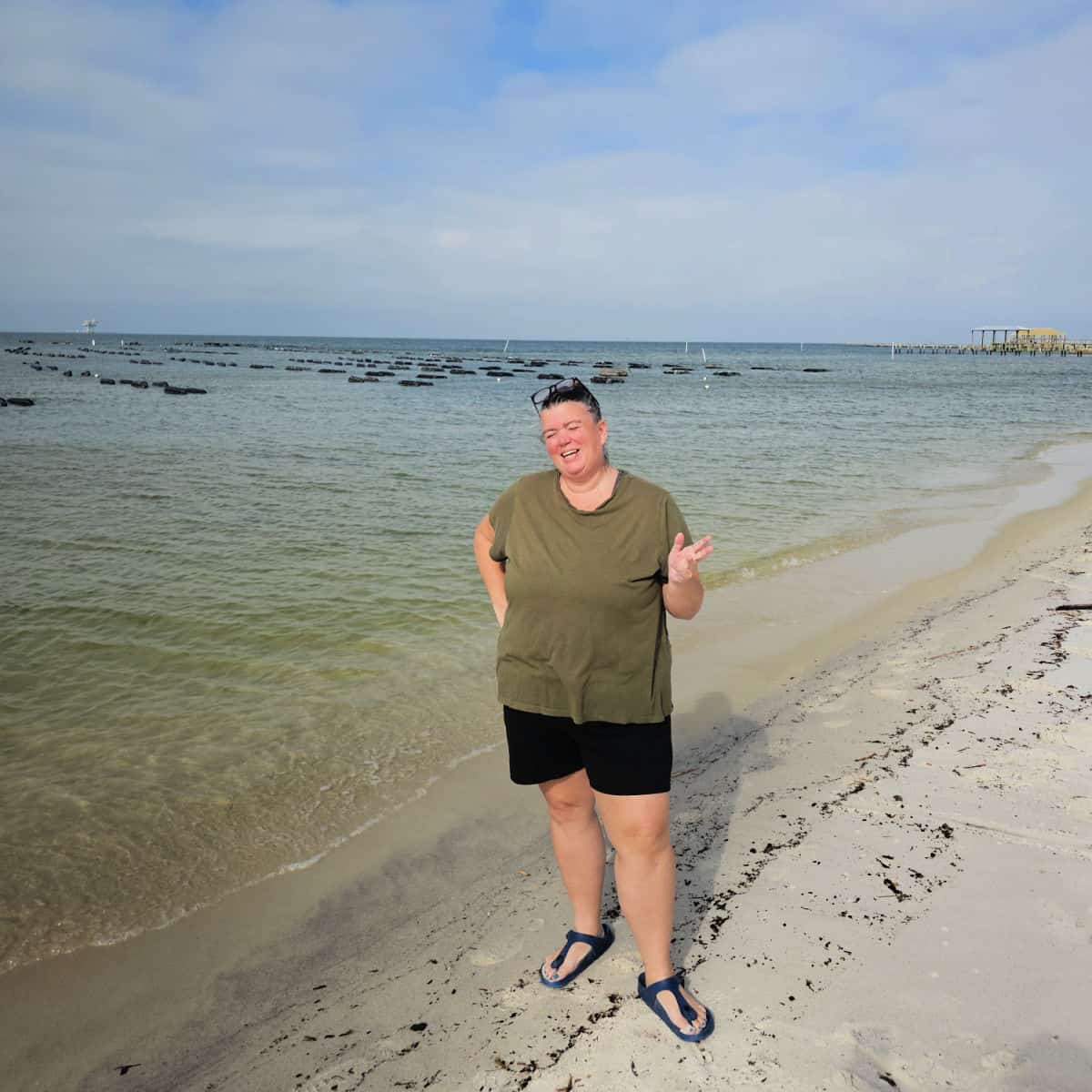 Tammilee standing on the beach laughing with Admiral Shellfish Company oyster farm in the background