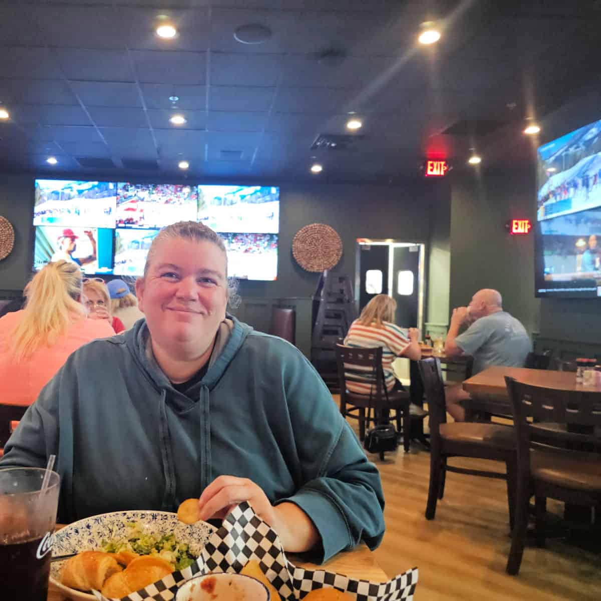 Tammilee with large tv's behind her, salads and chips on the table