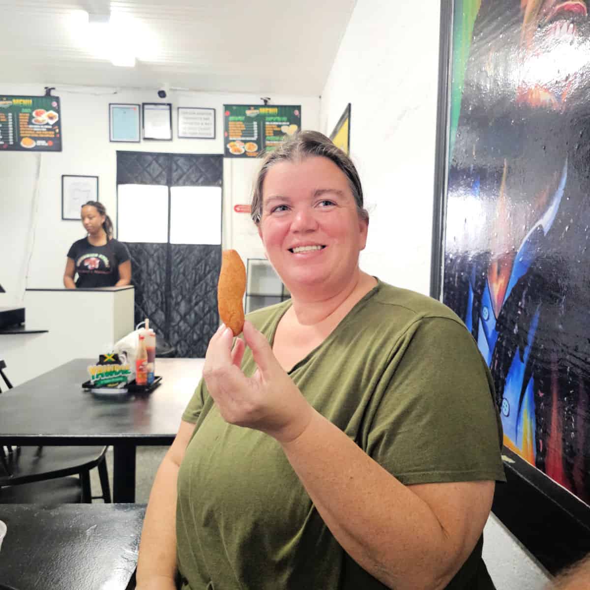 Tammilee holding a piece of festival bread at Yawdie in Foley with a painting behind her