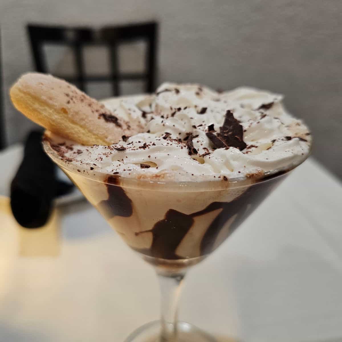 tiramisu martini with lady finger garnish in a martini glass on a white linen covered table