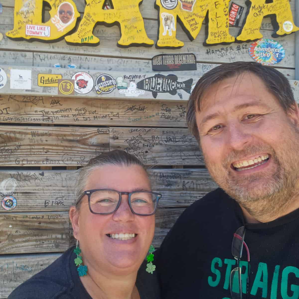 Tammilee and John at Flora Bama with a Gulf Coast Journeys sticker on the wall