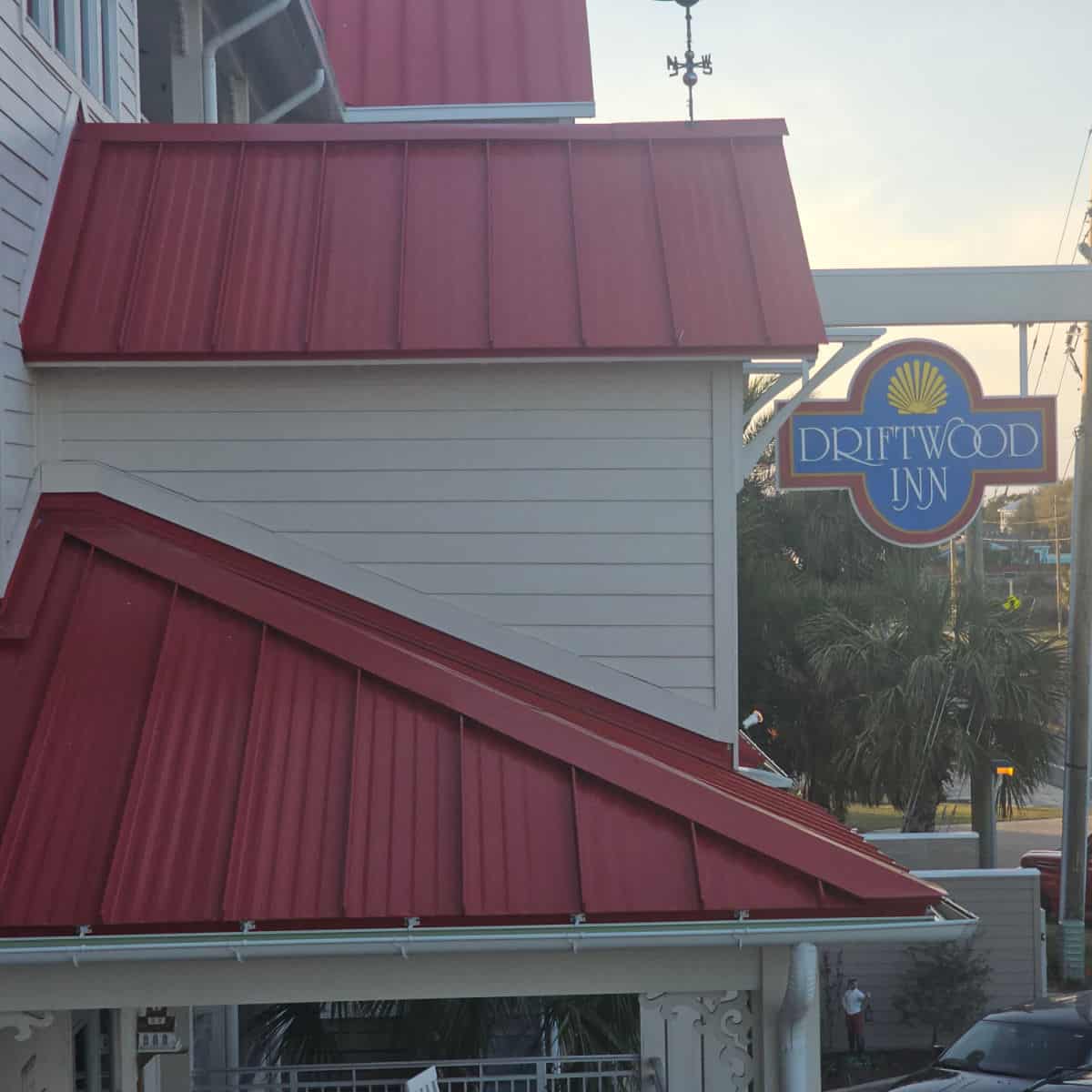 Drfitwood Inn sign hanging next to a white and red roof hotel