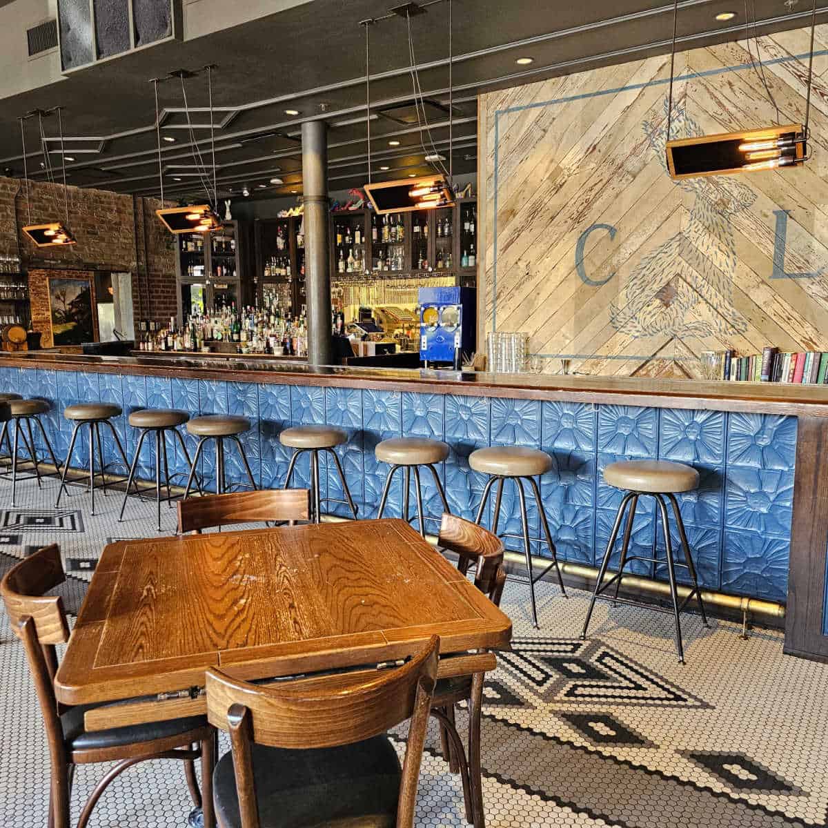 Compare Lapin bar area with blue tile wall by the bar stools, C L with a blue bunny painted on the wall and fully stocked bar