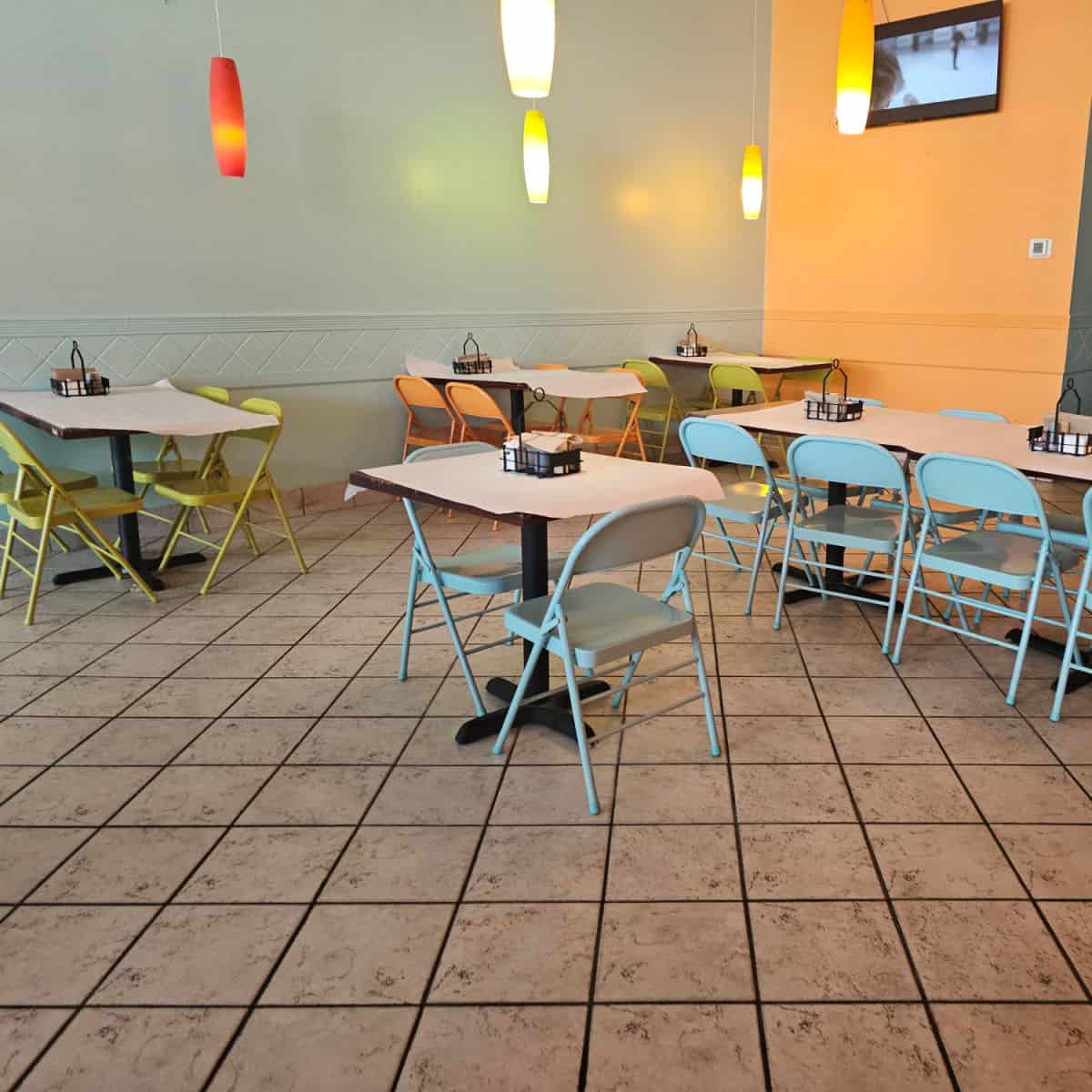 beli deli restaurant with green orange wall, tables covered in paper with folding chairs in different colors