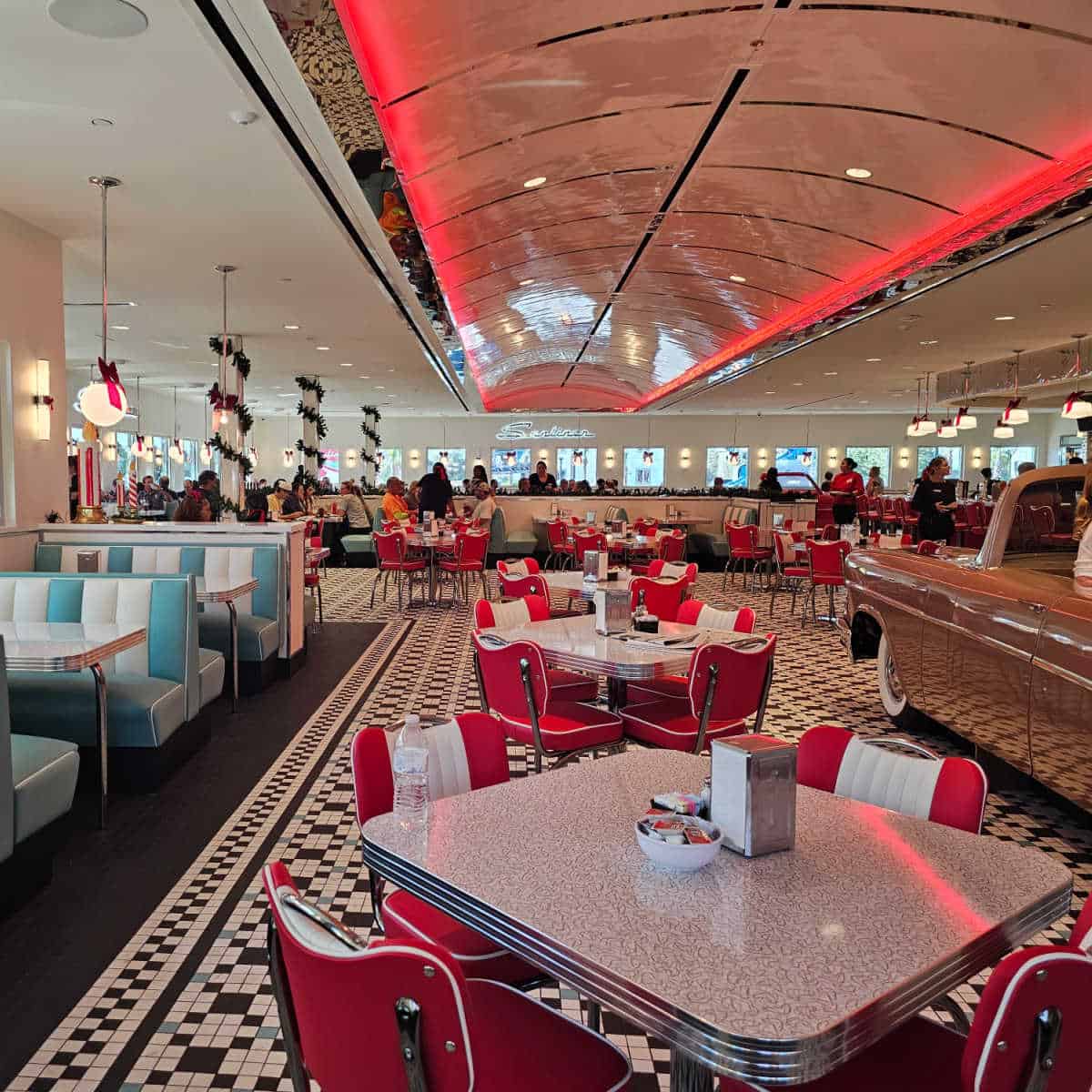 Sunliner diner interior seating with striped booths on the left, tables and chairs down the middle and a pink car on the right side