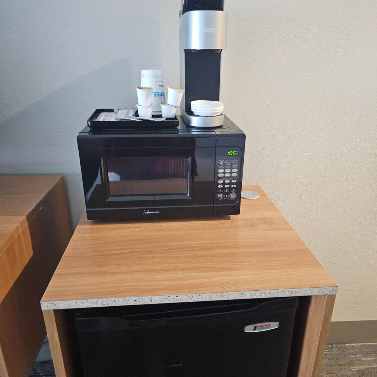 mini fridge in an open cabinet, small microwave on top with a keurig and k-cups next to it in a hotel room