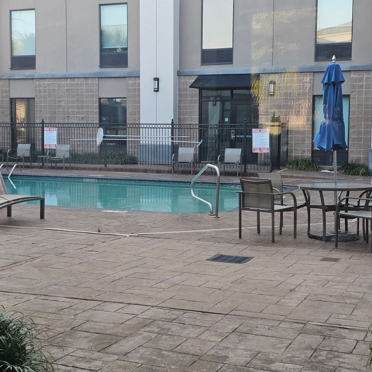 outdoor pool area with tables and chairs, umbrella down at the table, and gate around the pool