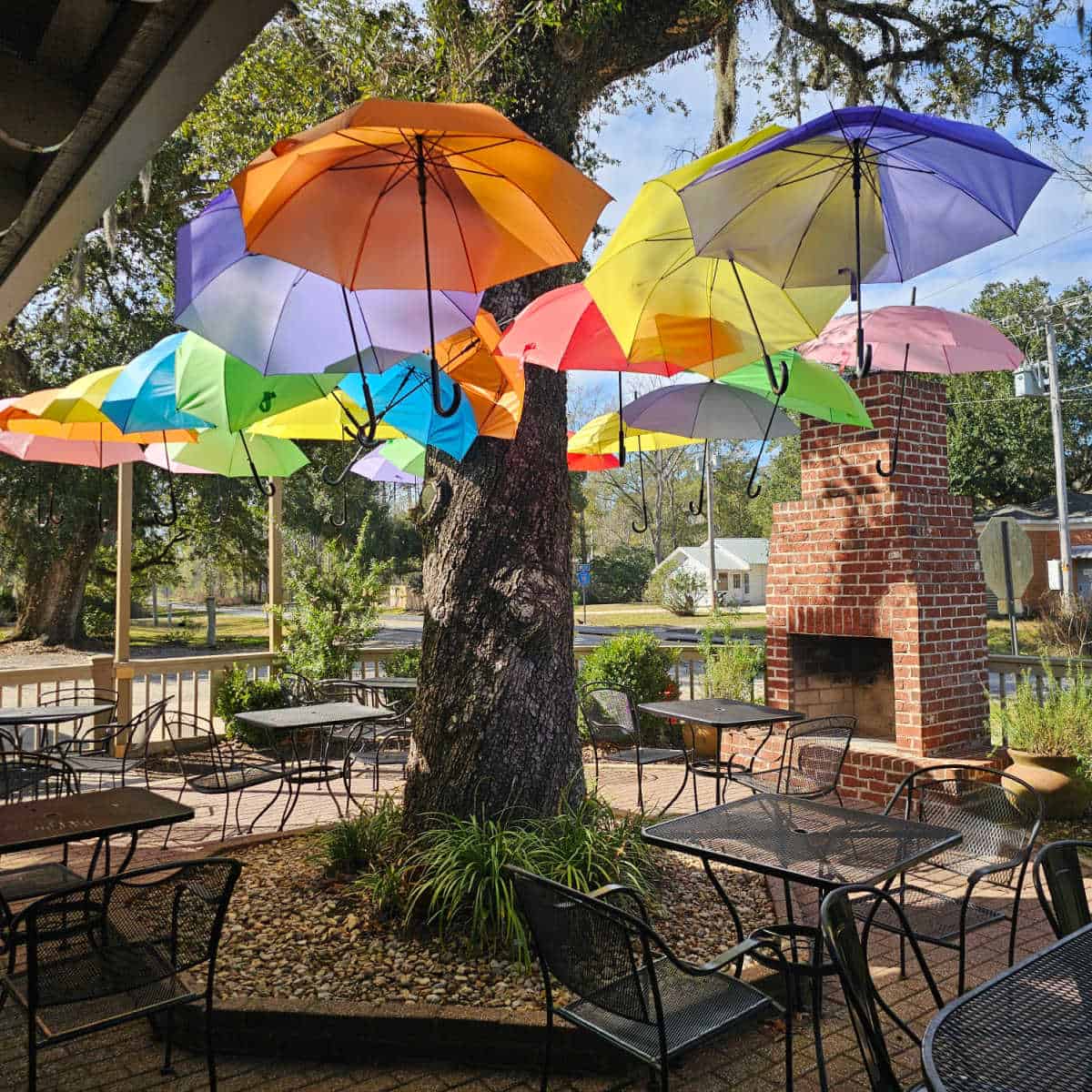 umbrellas hanging over tables with an outdoor fireplace and trees