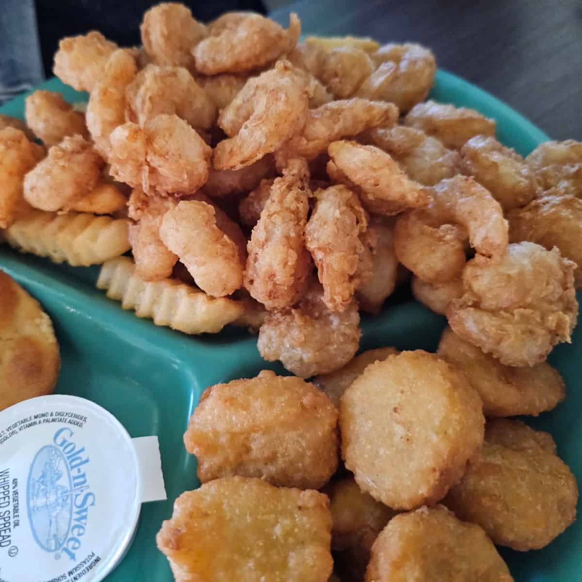 Popcorn shrimp, a couple french fries, and corn nuggest on a turquoise plate