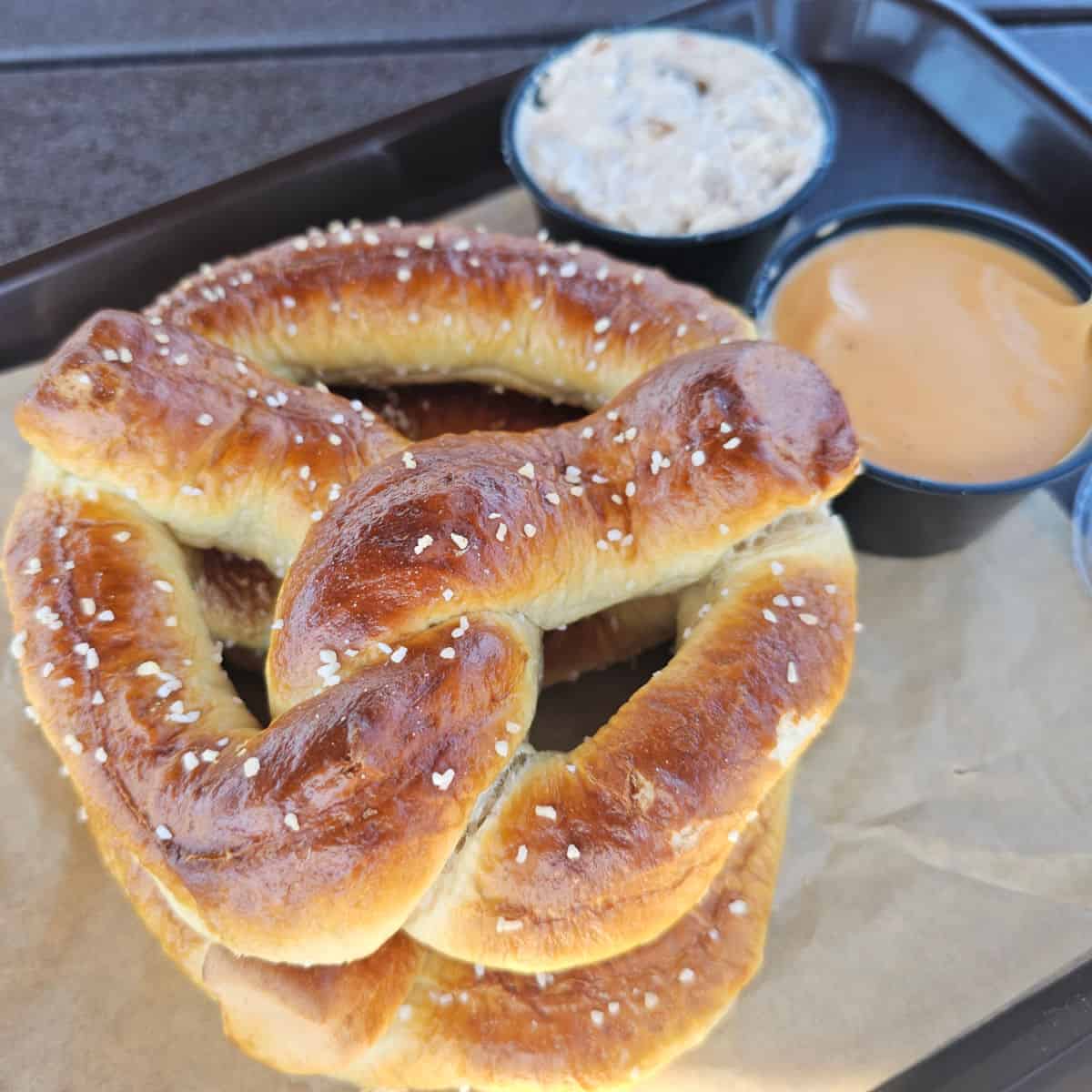 Pretzel on a tray with a container of beer cheese dip and a container of creamy dip
