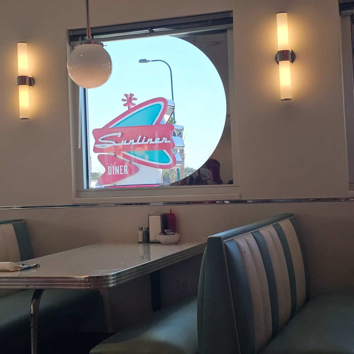 looking through the window over a booth with striped booth seats to the Sunliner Diner sign