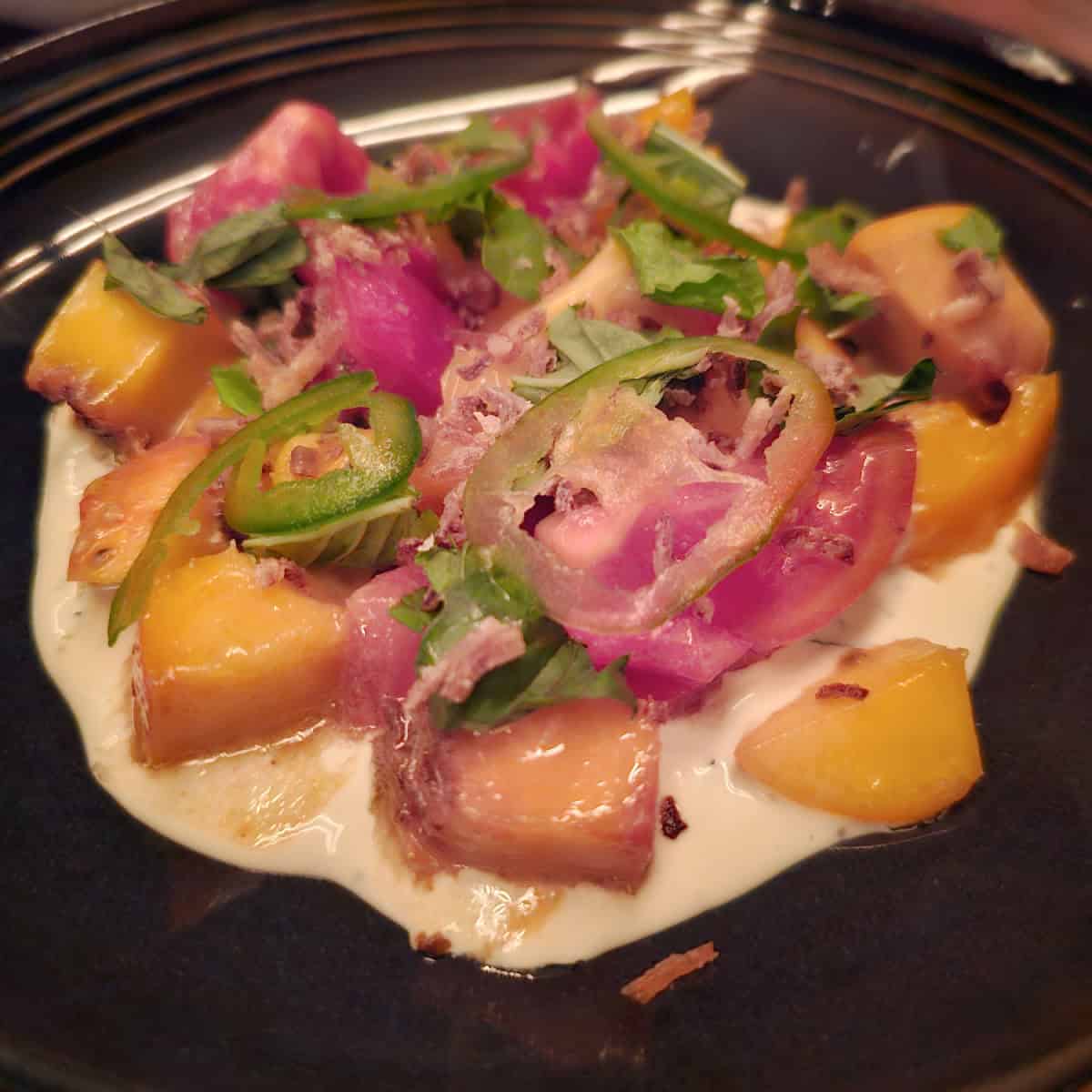 tomato salad on a dark plate with jalapenos and peaches