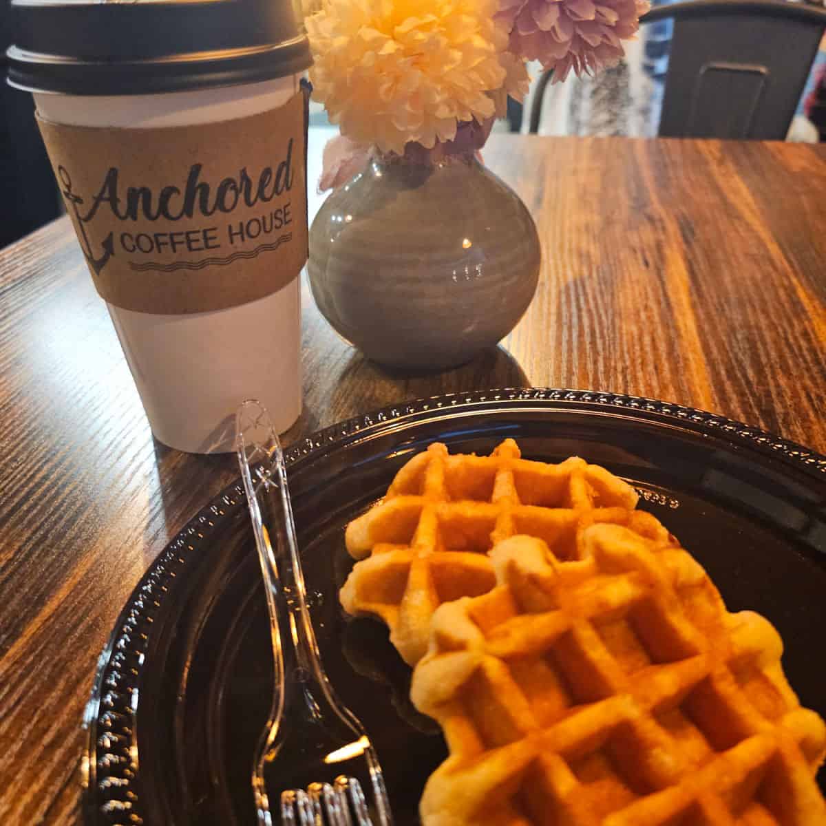 Anchored Coffee House Cup next to a plastic plate with two waffles on it