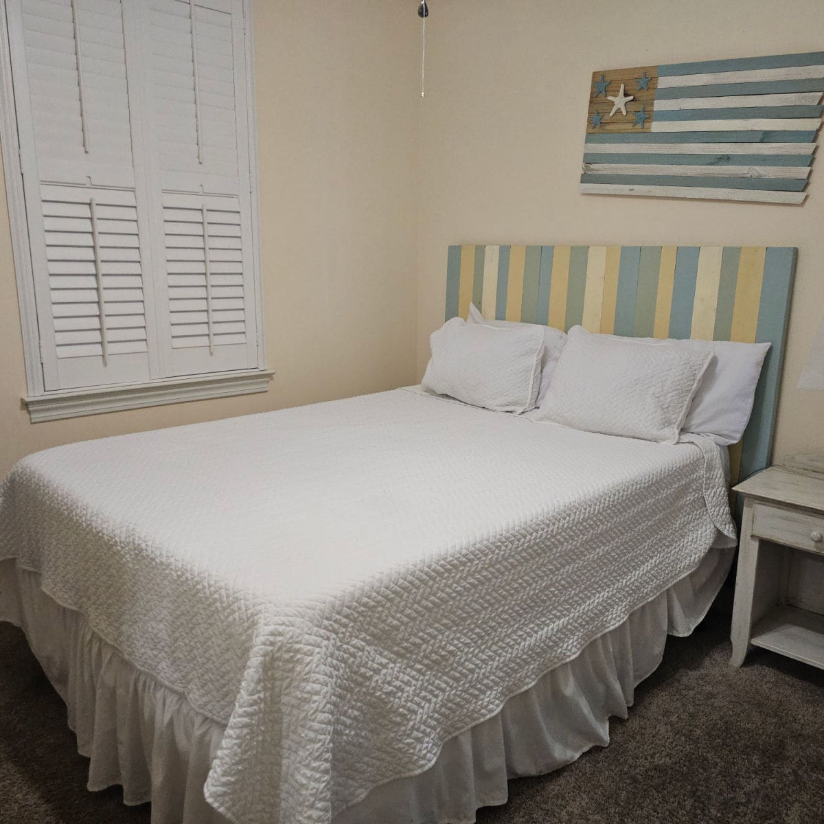 bedroom with white linens, striped headboard, flag art over head