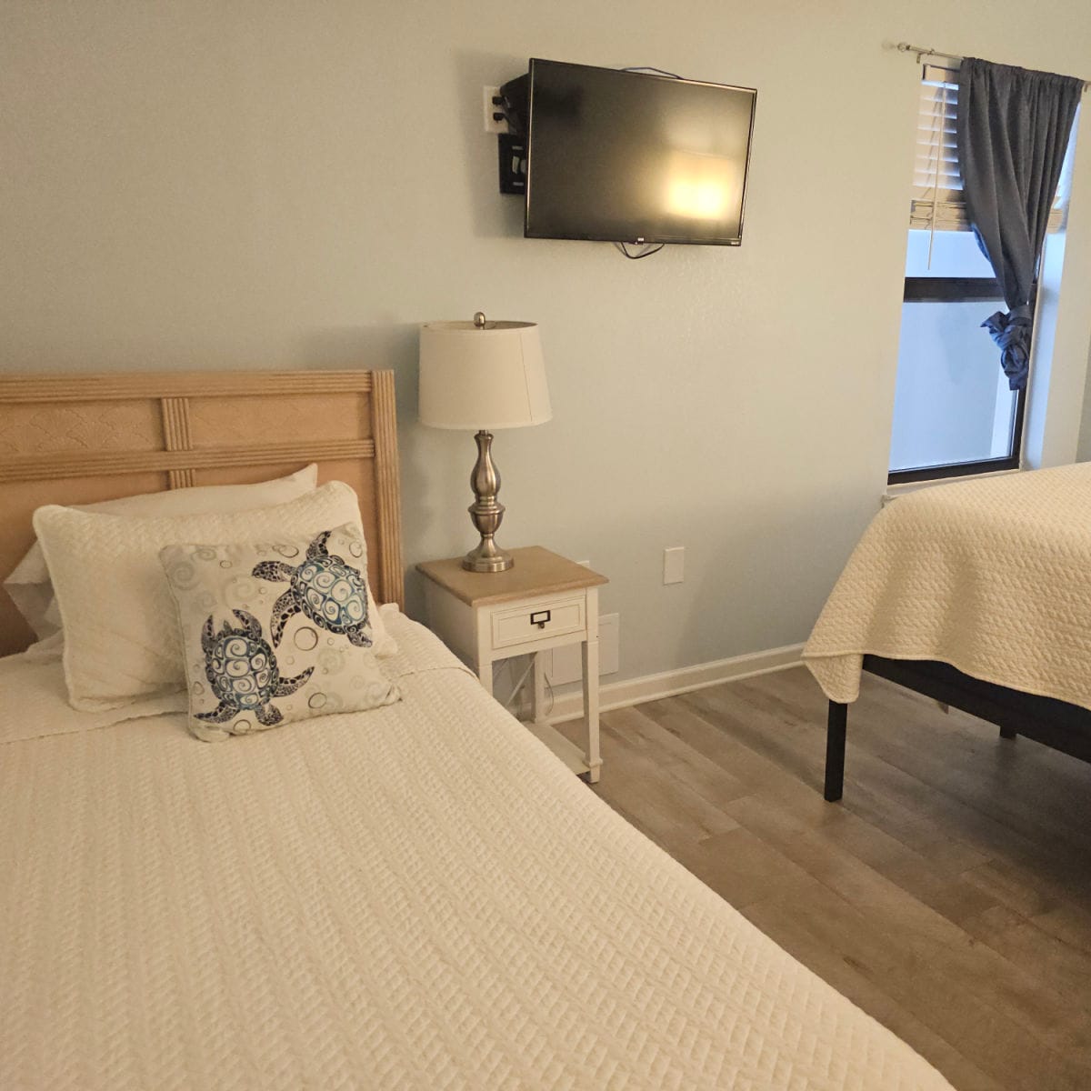 bedroon with two beds, white linens on the bed, flatscreen tv on the wall
