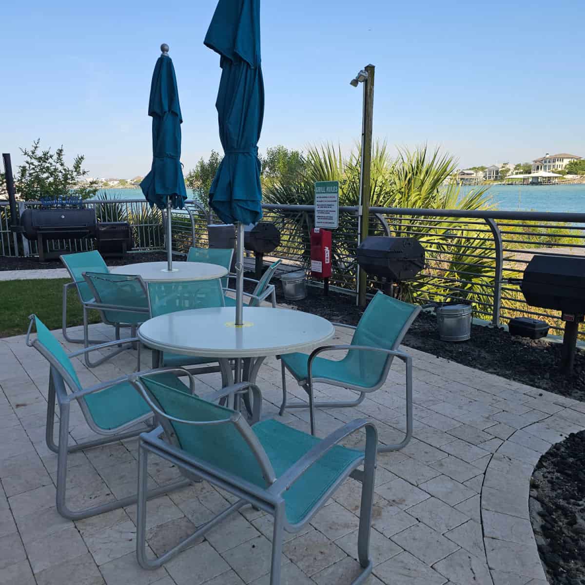 barbecue area with tables and chairswith blue umbrellas, water in the background