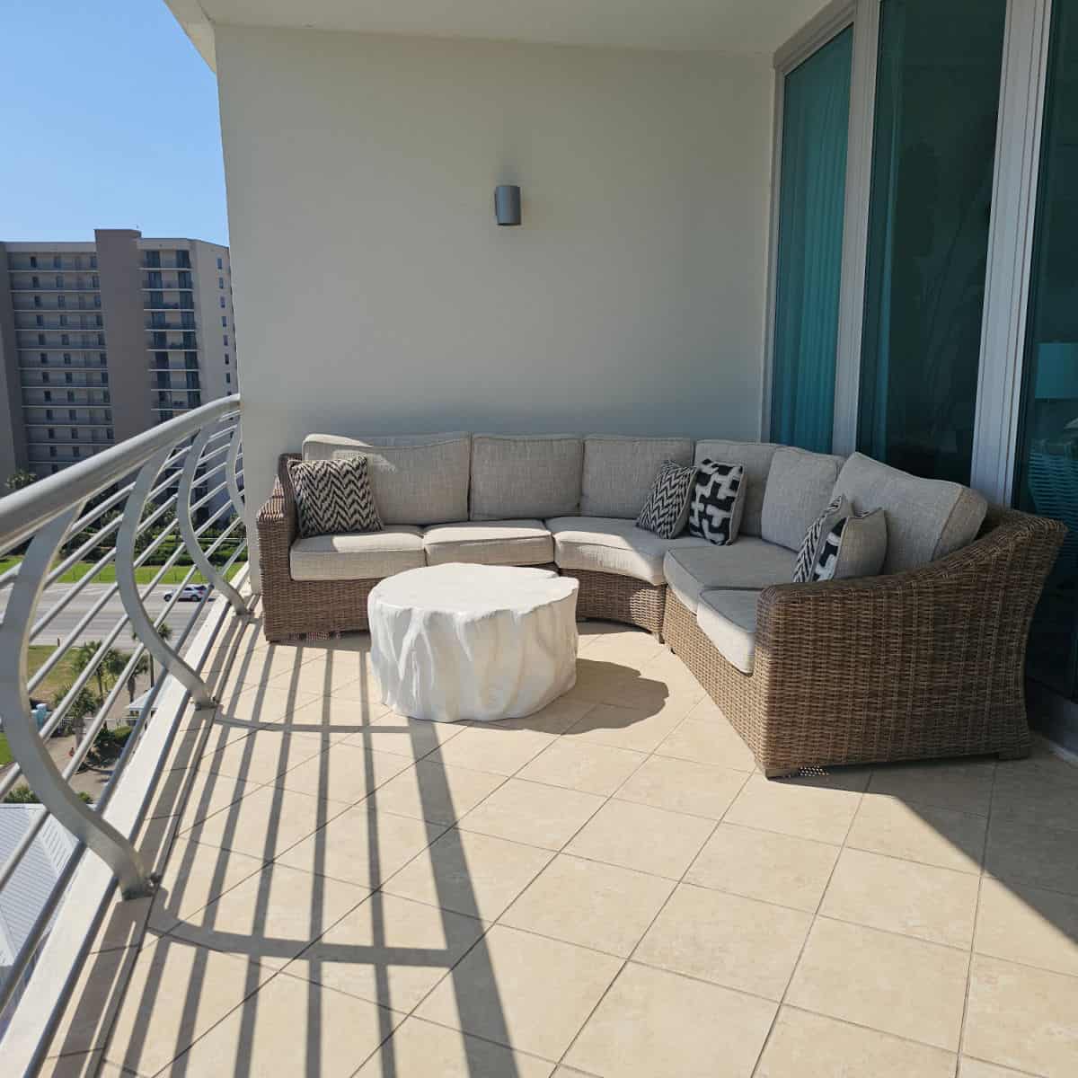 Balcony with large curved couch with pillows, white outdoor table