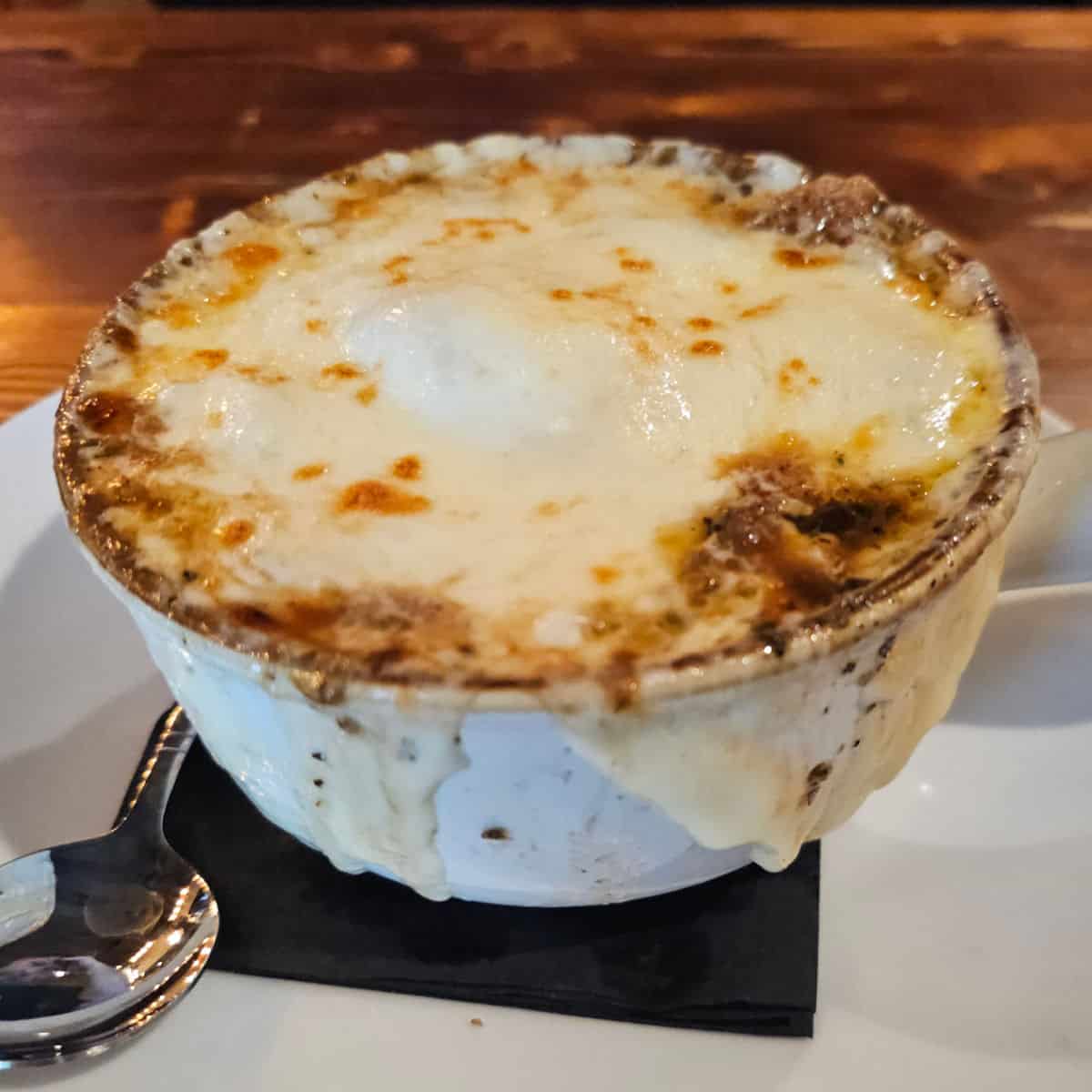 Cheese covered bowl with silver spoon on a white plate