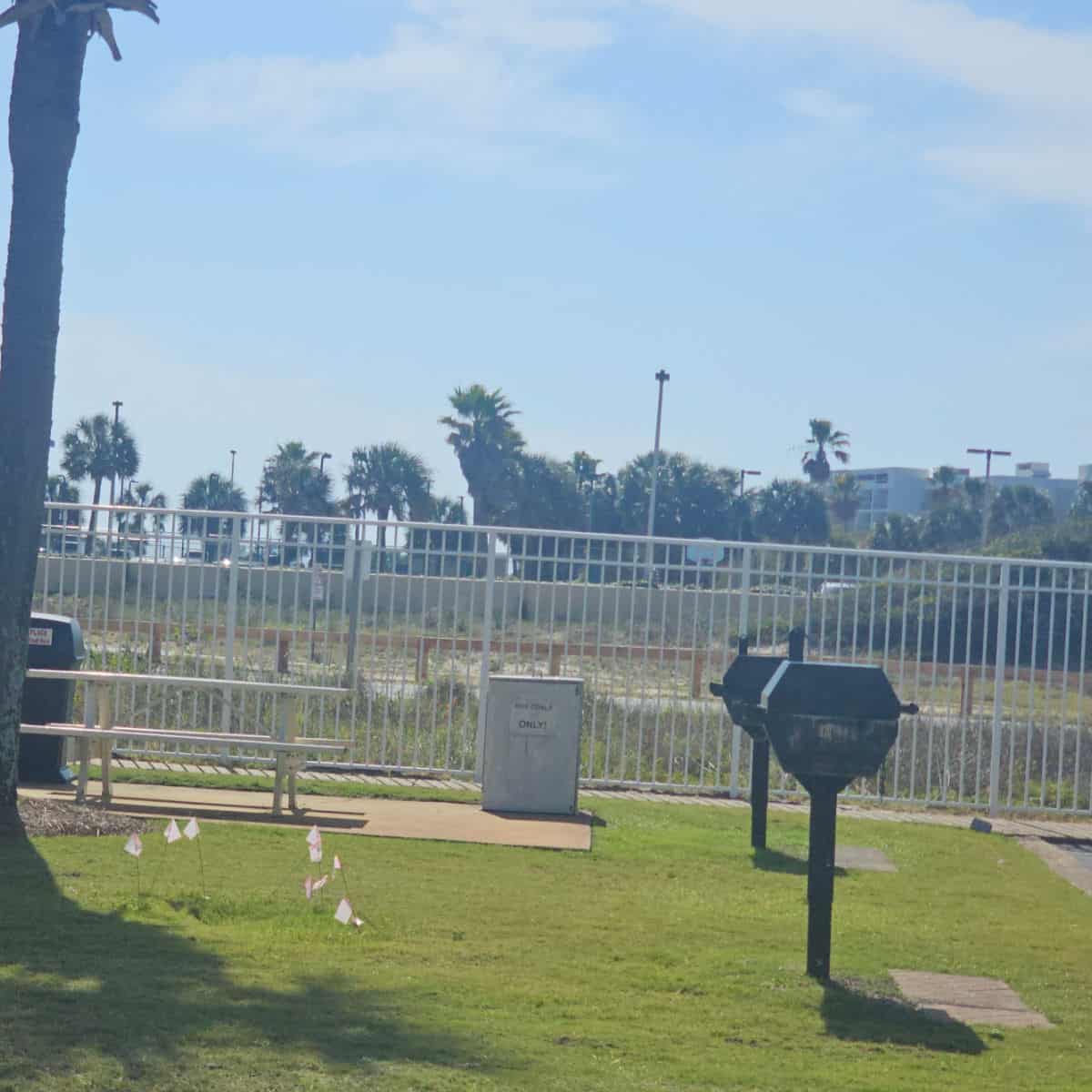 barbecues and picnic tables near a white fence