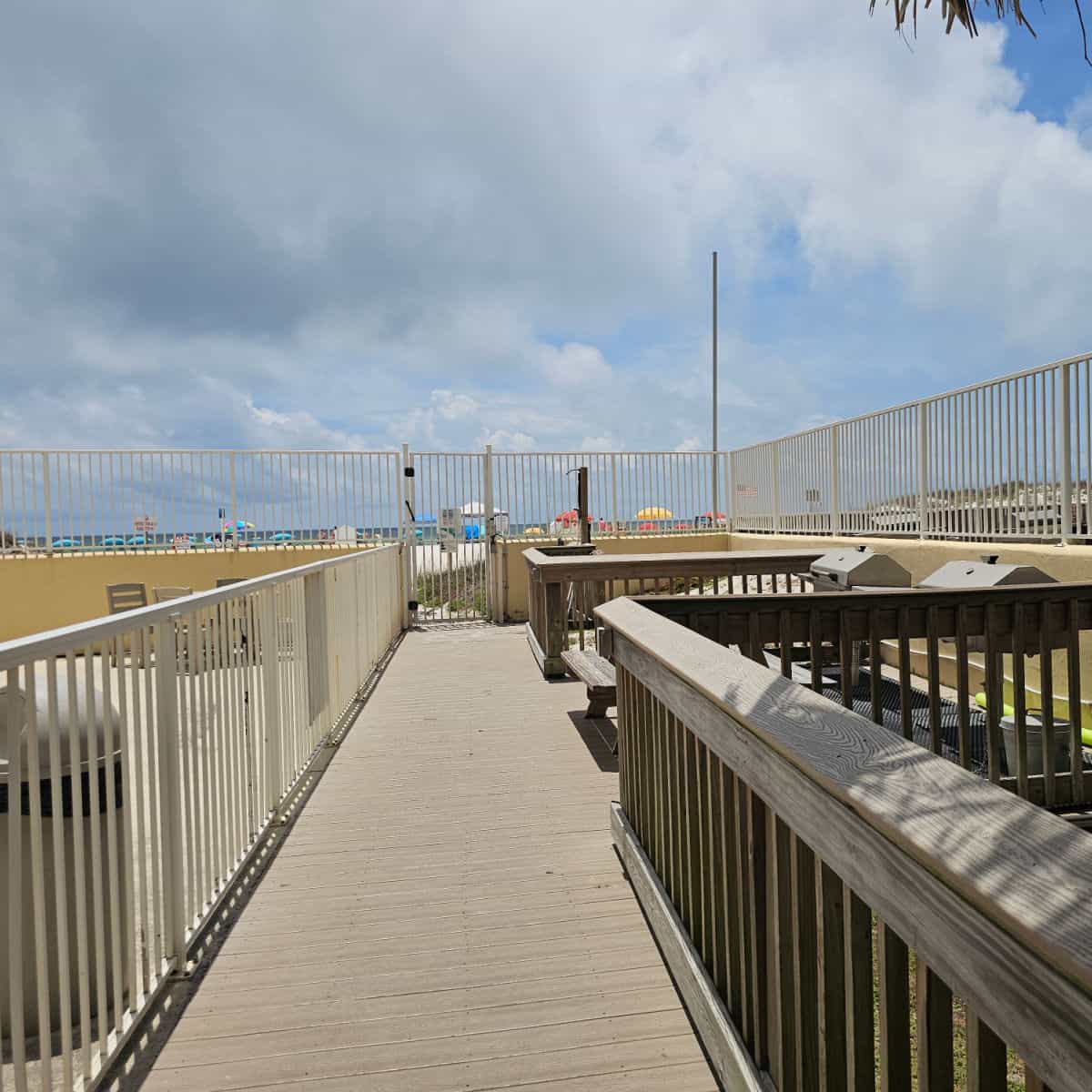 wooden boardwalk to a gate leading to the beach, two barbecues on the side