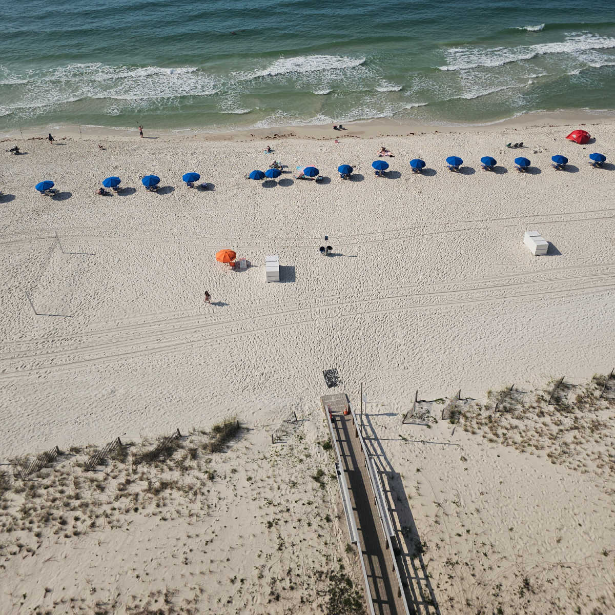 looking down on boardwalk leading to the beach, blue umbrellas lining the beach