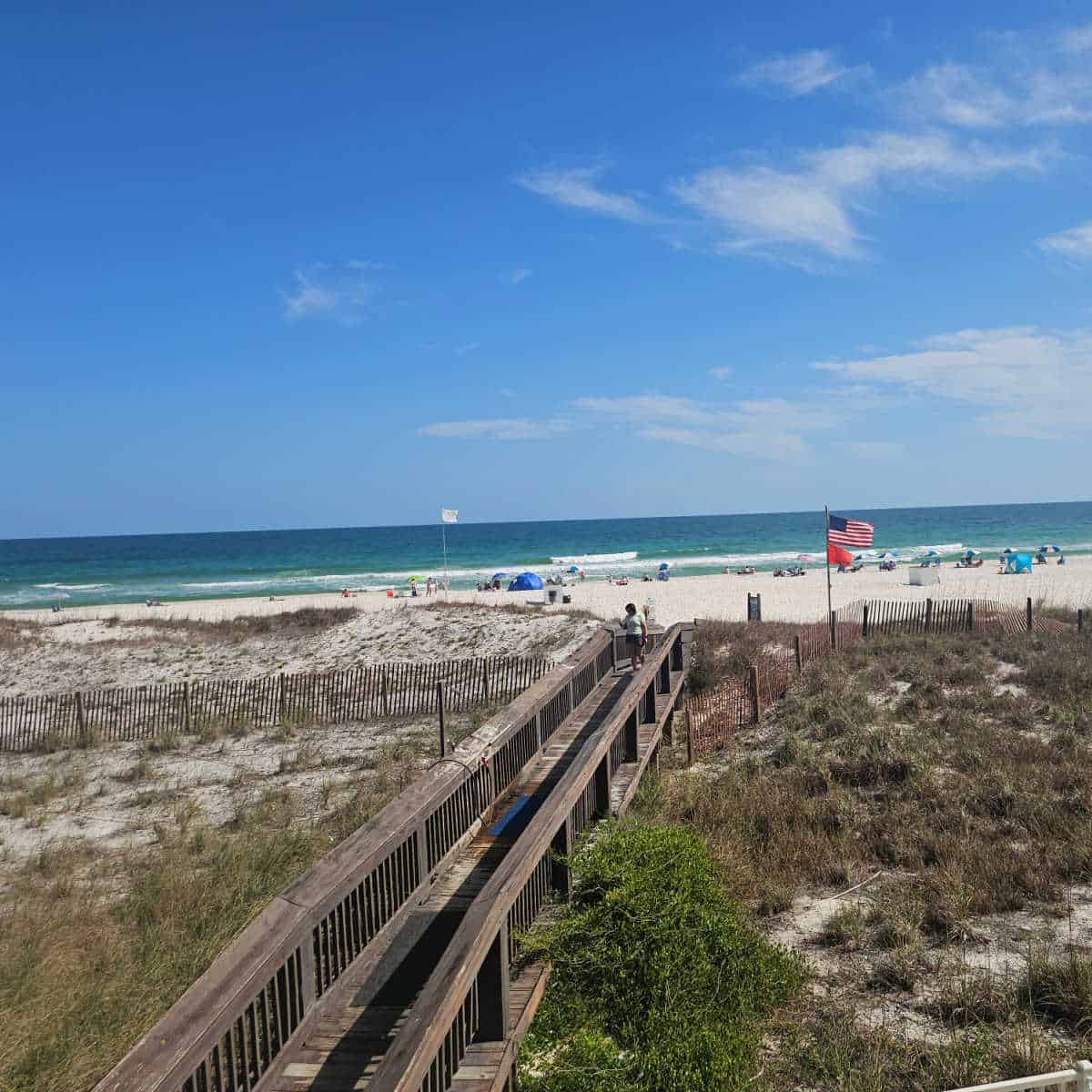 wooden boardwalk over and dunes to the white sand beach with the Gulf of Mexico in the background on a sunny day.