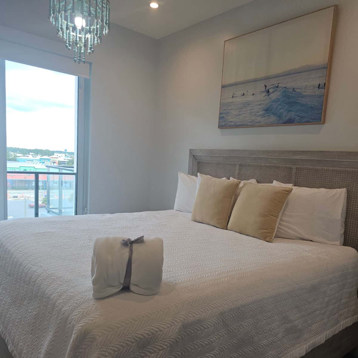 Bedroom with white linens, blanket folded in the corner, surfer picture on the wall and chandelier
