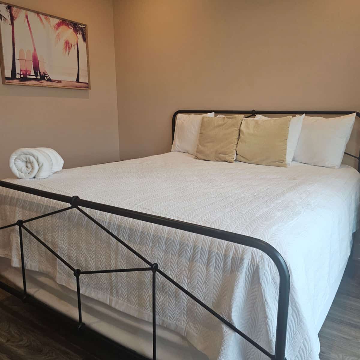 Bedroom with white linens, black bed frame, blanket folded in the corner, surfboard image on the wall at Gulf Place Condos