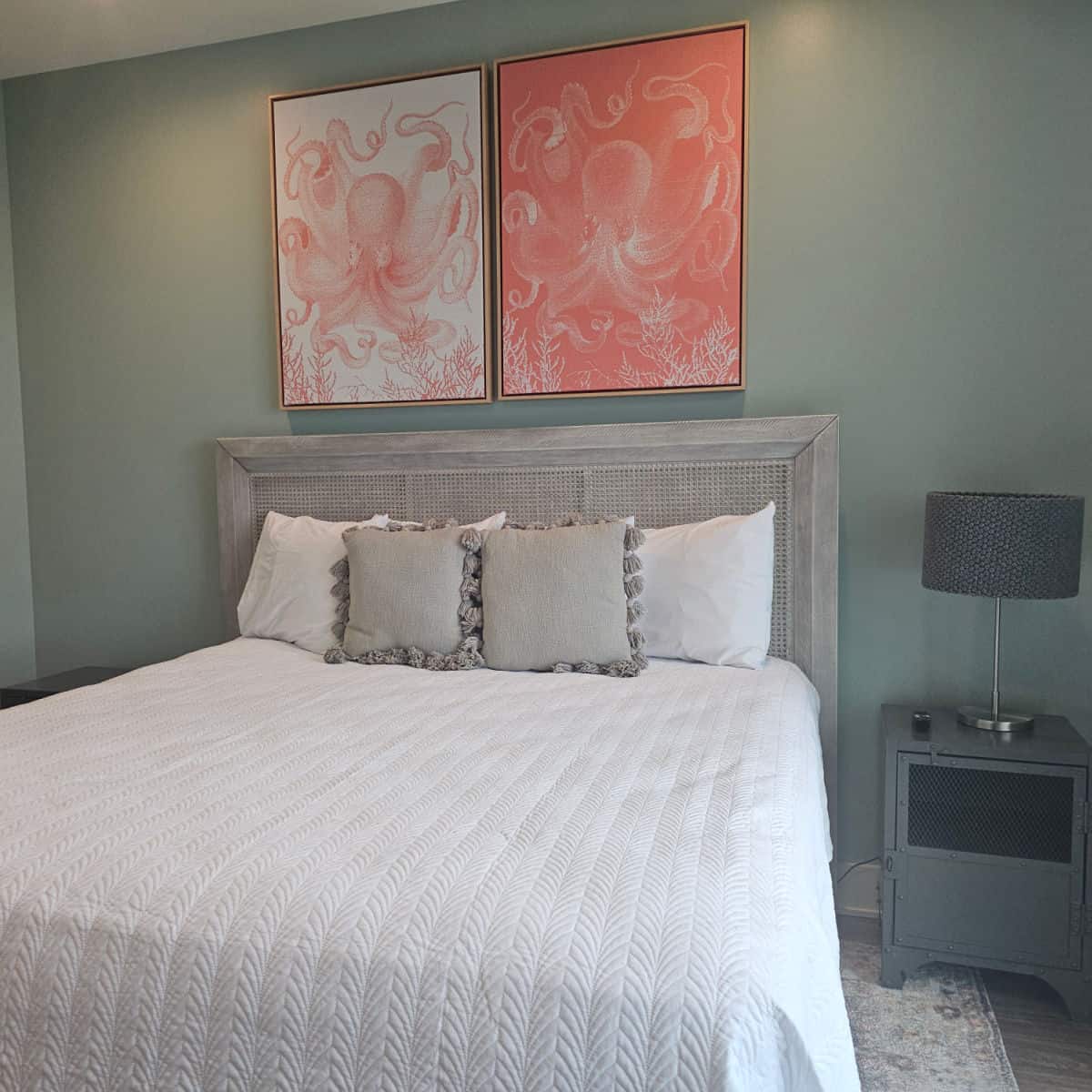 Bedroom with large bed with white linens and grey pillows, nightstand and lamp, two octopus prints on the wall