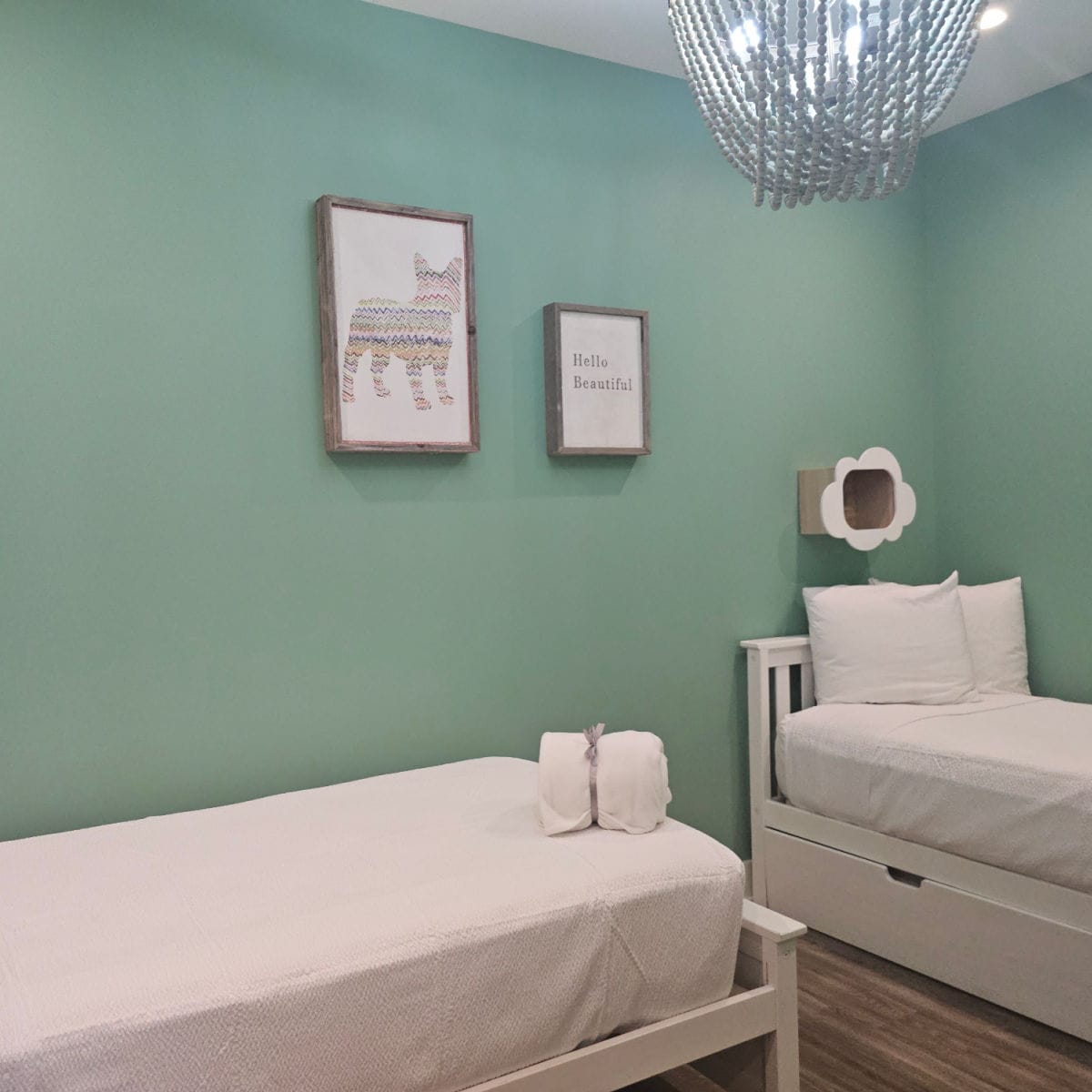 Bedroom with two twin beds, cubby on the wall, two prints and blanket folded on the bed