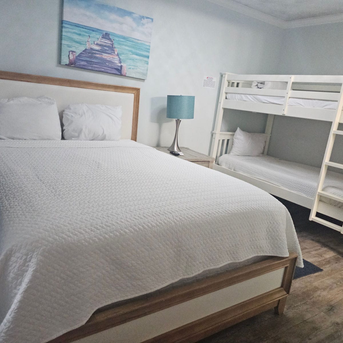 bedroom with a large bed with white linens next to a bunk bed, art on the wall