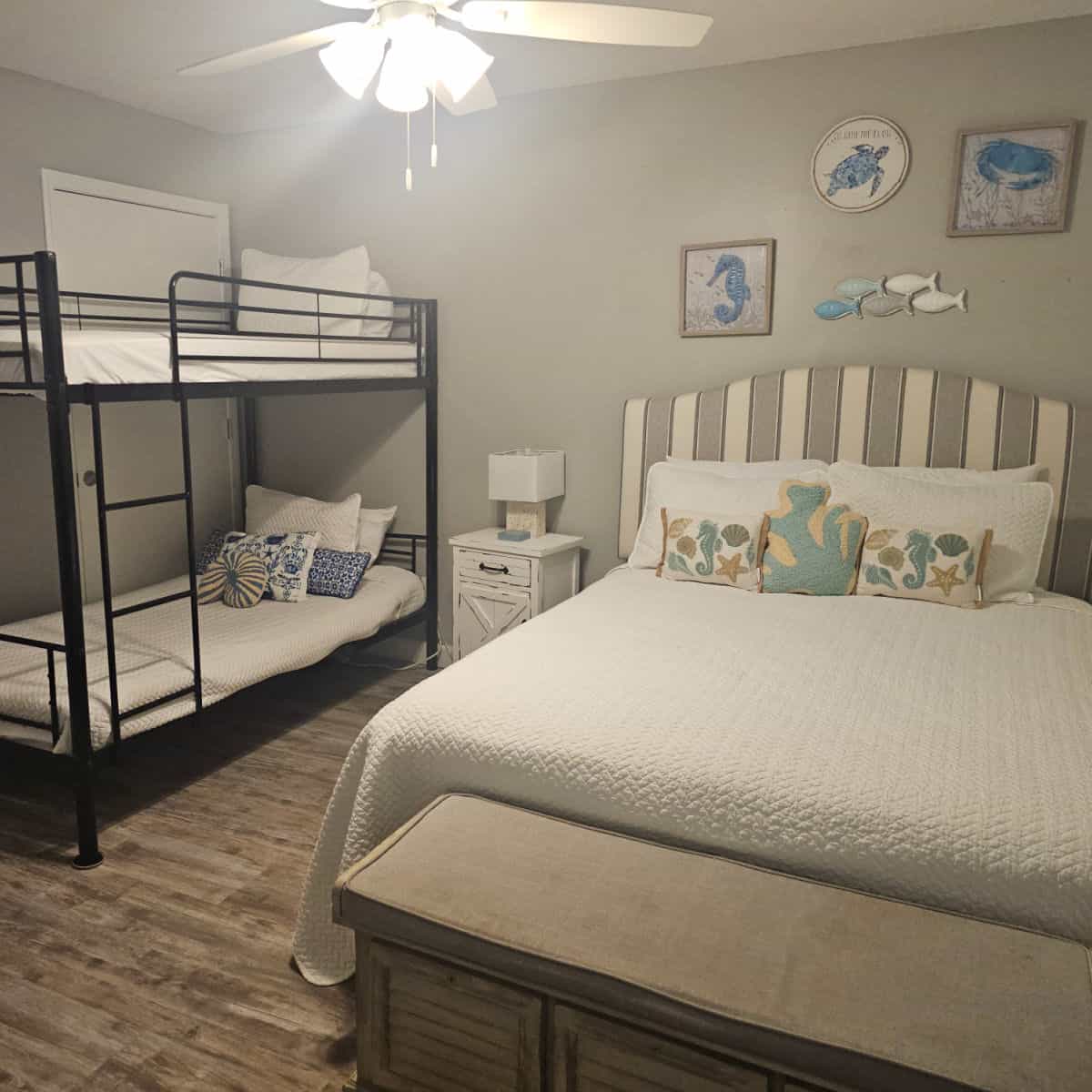 Bedroom with a bed and a bunkbed, coastal fish and sea horse art on the wall.