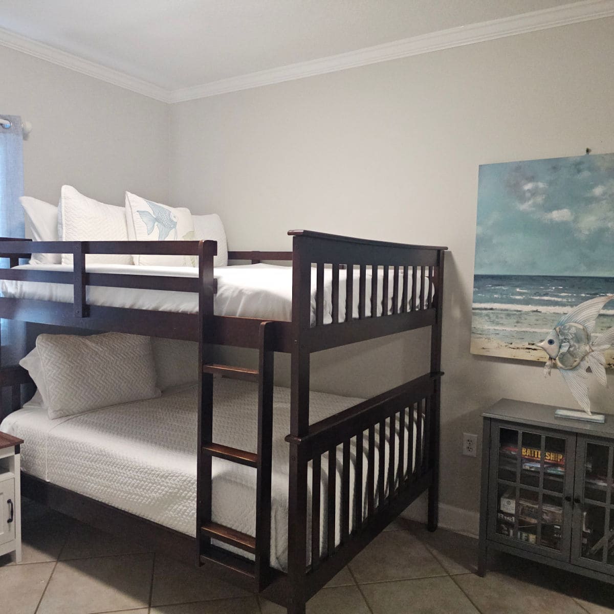 bunk beds with white linens and pillows, blue art on the wall, and cabinet