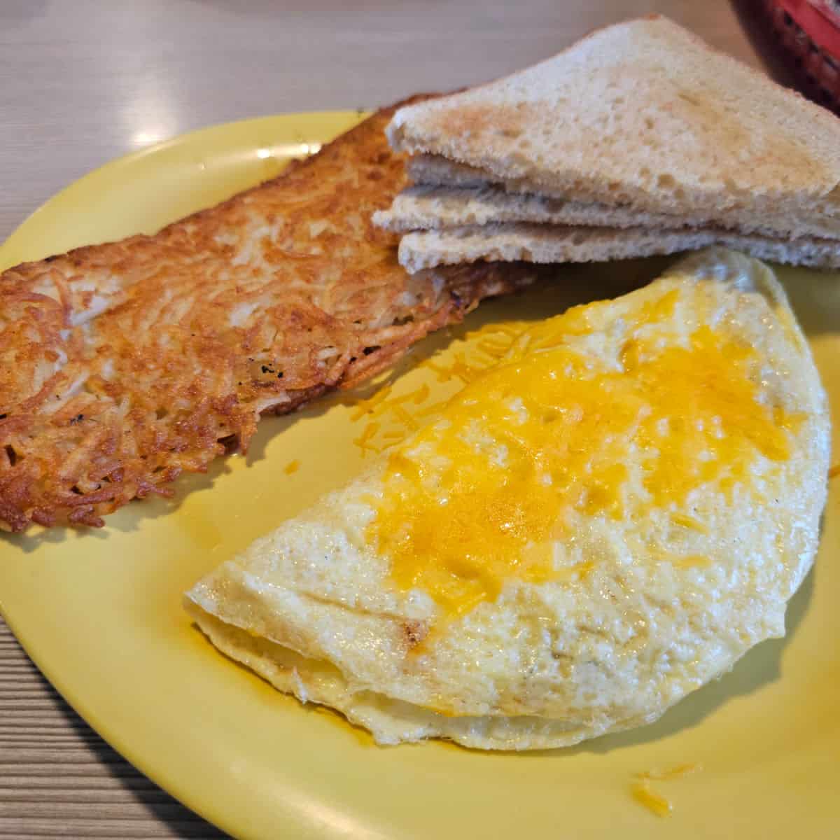 cheese omelet next to hashbrowns and toast on a yellow plate