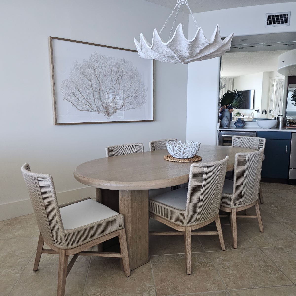 dining room with light brown oval tables, chairs around the table, white chandelier, art on the wall,