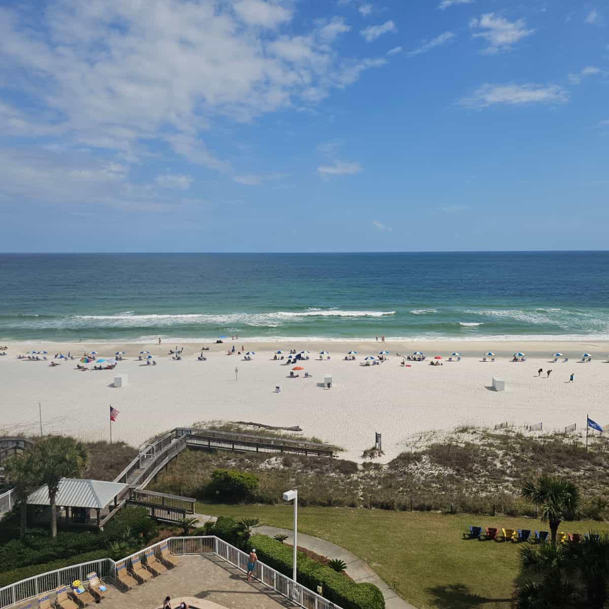 looking over a pool deck to beach path, sandy beach and Gulf waters on a blue sky day