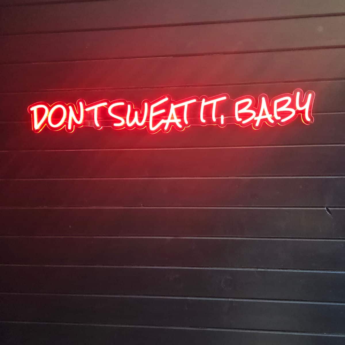 Don't sweat it baby red neon sign on a dark wall