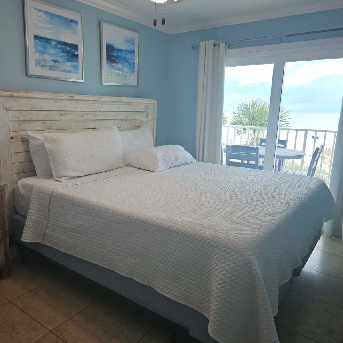 bed with wooden headboard and white linens, blue walls and art, gulf in the background