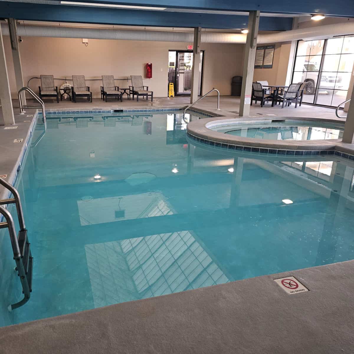Indoor pool and hot tub with lounge chairs against the back wall